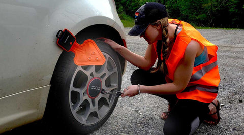 STKR Concepts' FLEXIT Auto in use attached to a car wheel well as a female wearing a safety orange vest works on the wheel.