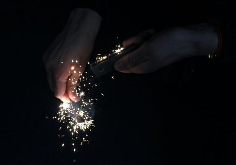 hands striking flint and steel together in the darkness creating lots of sparks