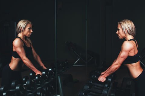 female looking in a gym mirror at herself as she goes to pickup free weights