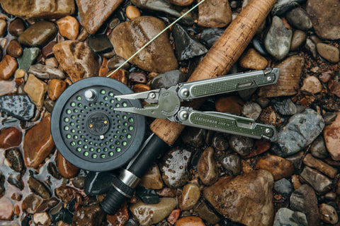 Multi-tool pliers sitting on top of a fishing pole in a wet river rock bed setting