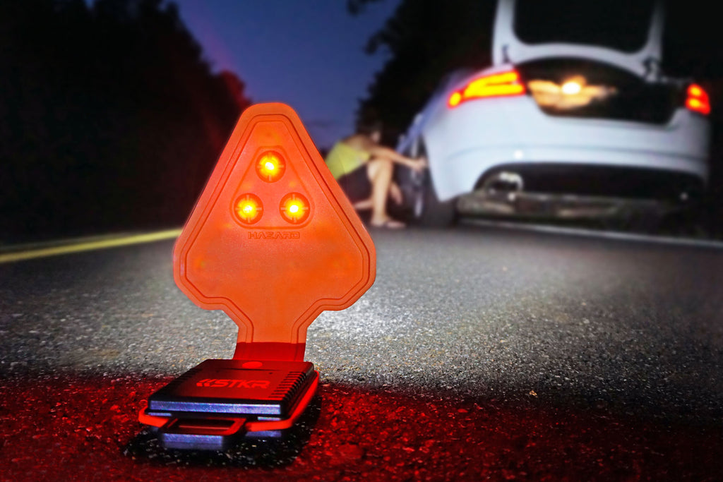 FLEXIT Auto flexible flashlight sitting in the road illuminating a white car that's pulled over with a female checking the rear tire