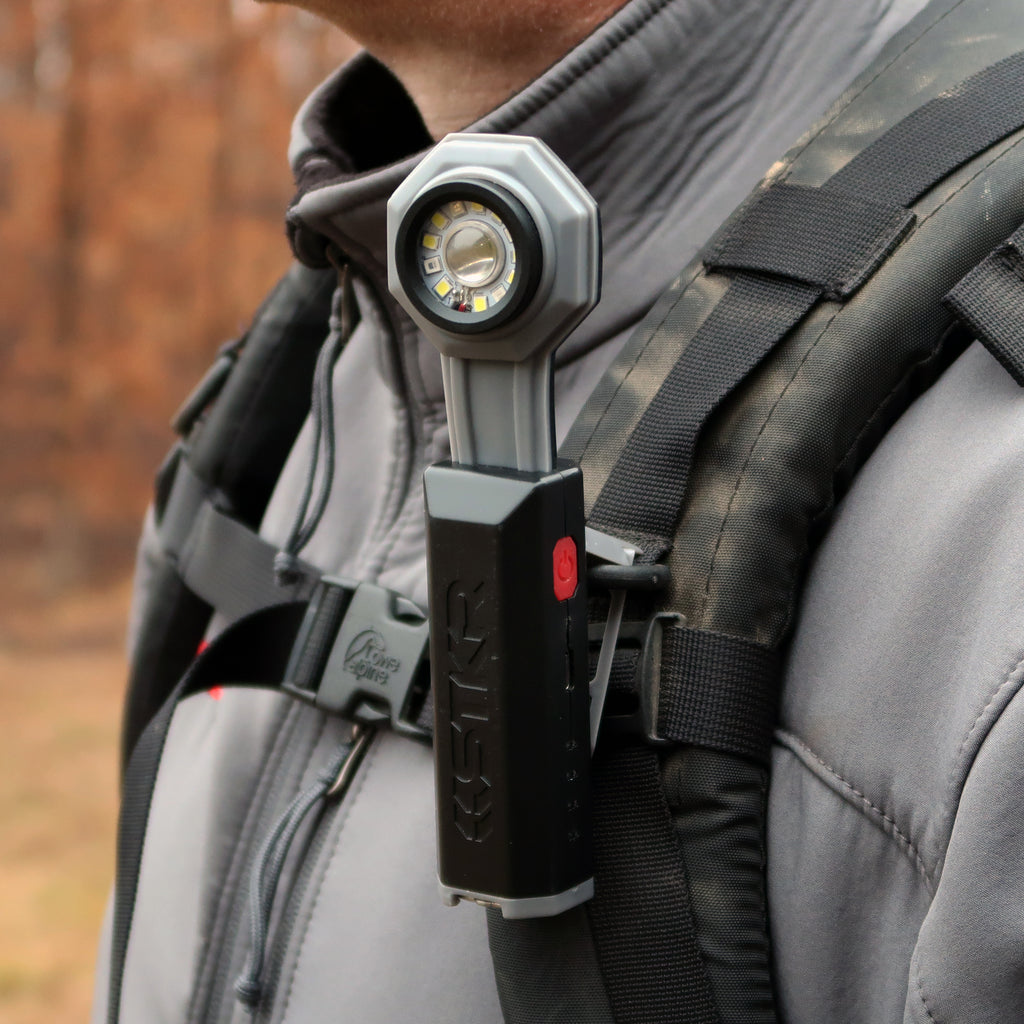 Close up of an STKR Concepts FLEXIT Pocket Flashlight clipped to a hikers backpack strap