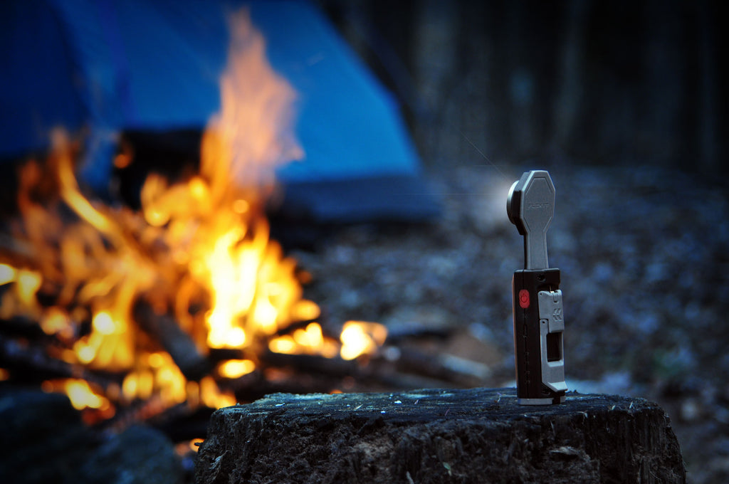 STKR FLEXIT Pocket Flashlight sitting on a tree stump overlooking a campfire