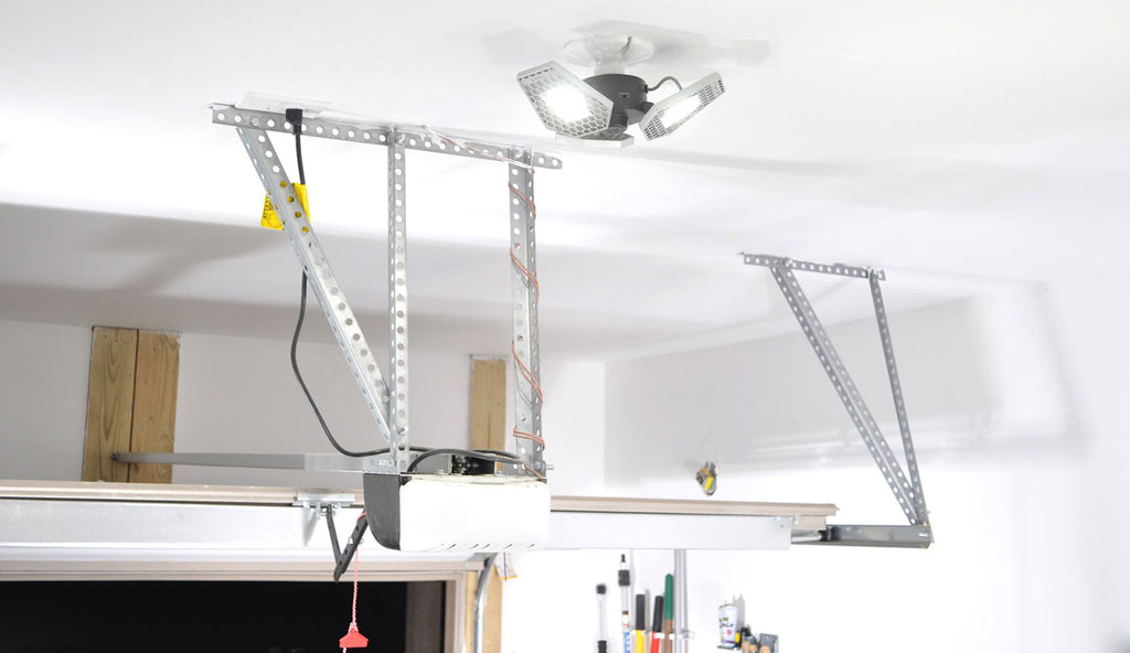 a trilight motion activated garage ceiling light shown screwed into a standard outlet in a white garage near the garage door opener