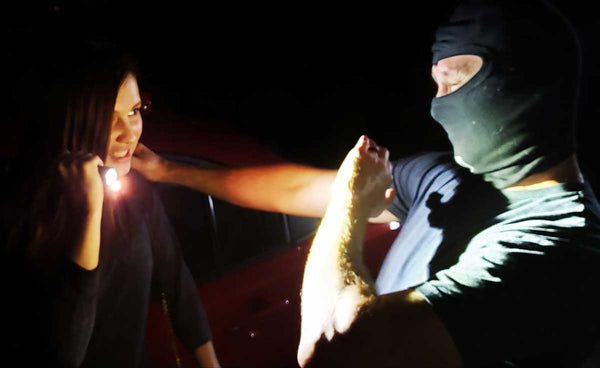 Woman defending herself with a tactical flashlight against a masked male attacker