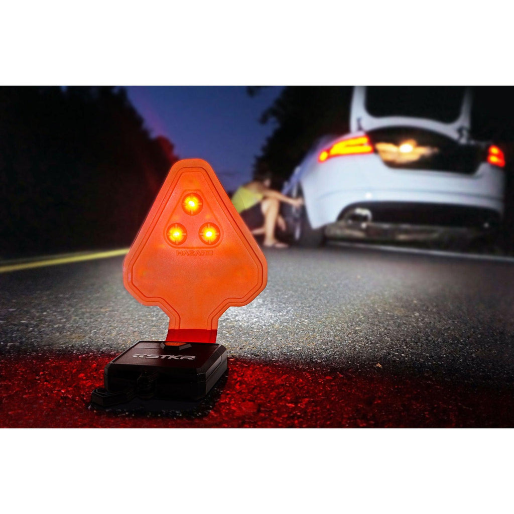 Un FLEXIT Auto sentado en la carretera por la noche iluminando un automóvil con una persona inspeccionando el neumático trasero borroso en el fondo