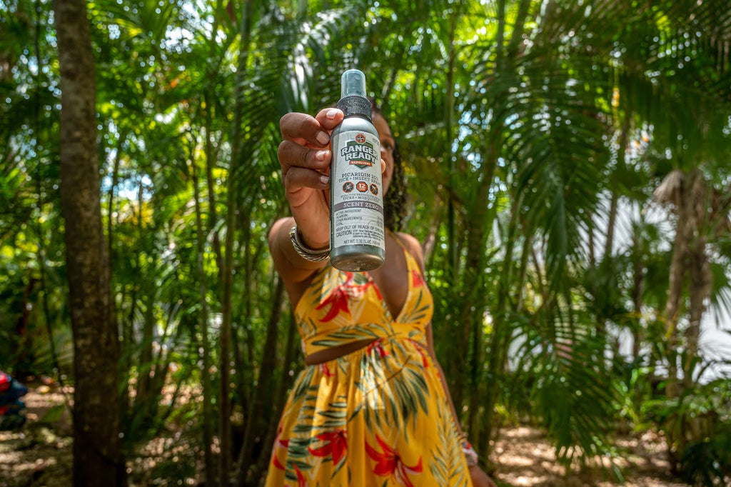 woman in yellow dress in the forest in the summer holding up ranger ready Picaridin 20% insect repellent to the camera