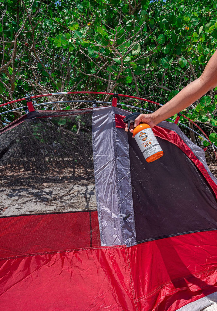 person spraying ranger ready permethrin repellent on a red tent on the beach