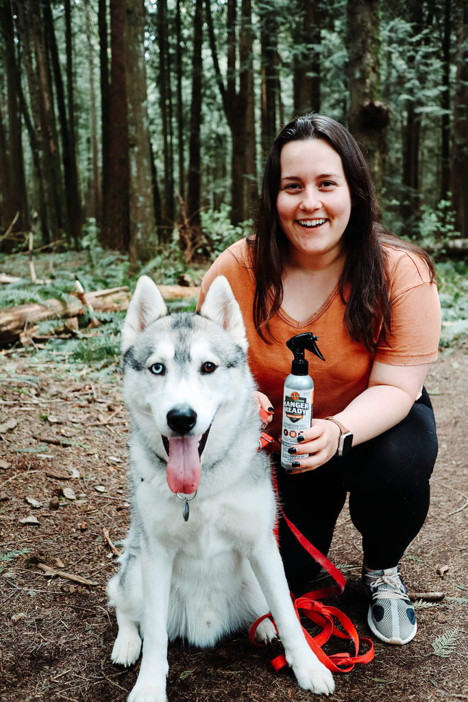 Woman of She Travels Blog and dog sitting in the woods holding up ranger ready Picaridin 20% bug spray