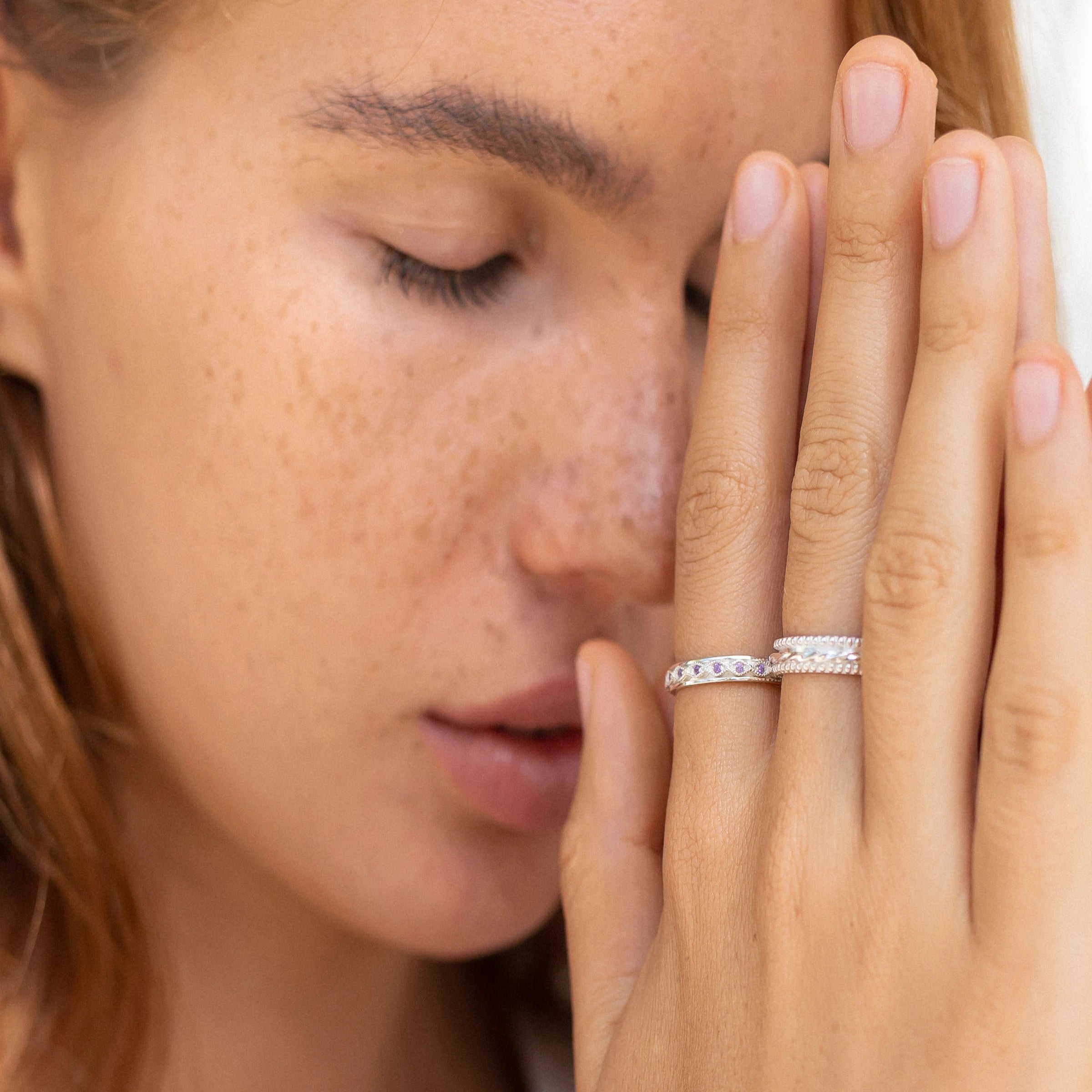 Close-up of a woman with eyes closed and hands in prayer position, wearing gemstone and silver spinner rings to relieve stress and promote calmness.