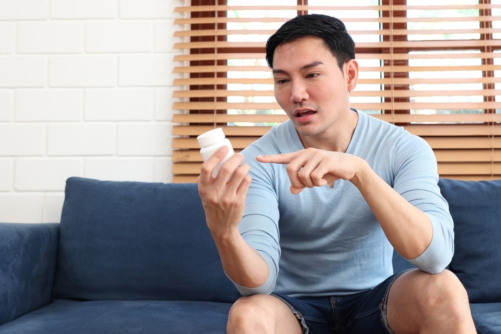 a man holding and reading instructions on white pill bottle