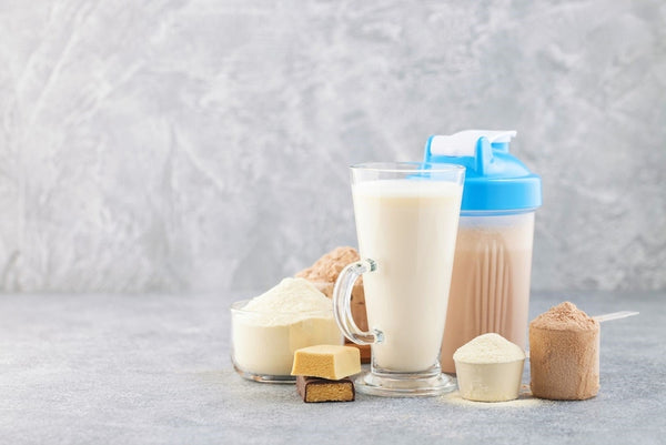 protein shake in glass and a tumbler surrounded by protein shake ingredients