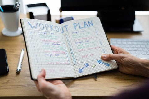 tips for building muscle growth - lean muscle mass - hands holding a notebook with handwritten workout plan