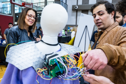 A woman and a man looking at computer wires on a mannequin