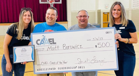 Two women wearing CAAEL t-shirts presenting award and check to two men