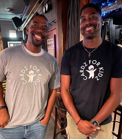 Two black men standing next to each wearing black and gray Cardz For Kidz t-shirts from CLOZTALK