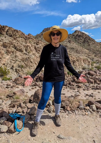 Woman hiking and wearing brim hat and sunglasses and smiling for camera with mountains in background