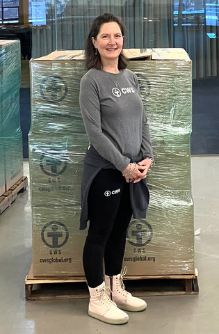 Woman wearing Church World Service gray long-sleeve t-shirt and black leggings in front a pallet