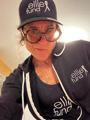 Woman wearing Ellie Fund black trucker baseball cap, black hoodie, and black tank top