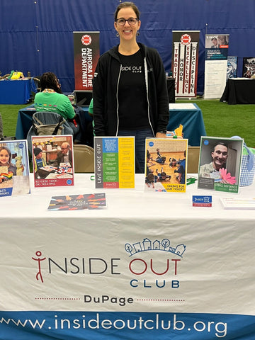 Woman wearing Inside Out Club DuPage black hoodie and black t-shirt standing in front of table with placards on it