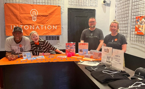 Four Intonation Music team members at table with placards and merchandise