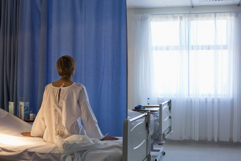 Woman patient sitting on hospital bed and looking out window