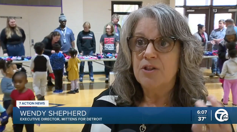 Executive Director of Mittens For Detroit speaking to TV reporter in school gym