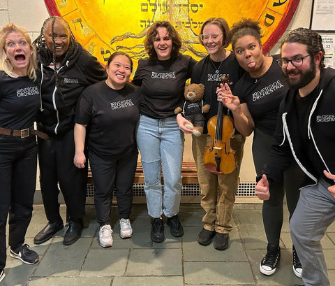 Six women and one man in The Riverside Orchestra black t-shirts and a hoodie posing together