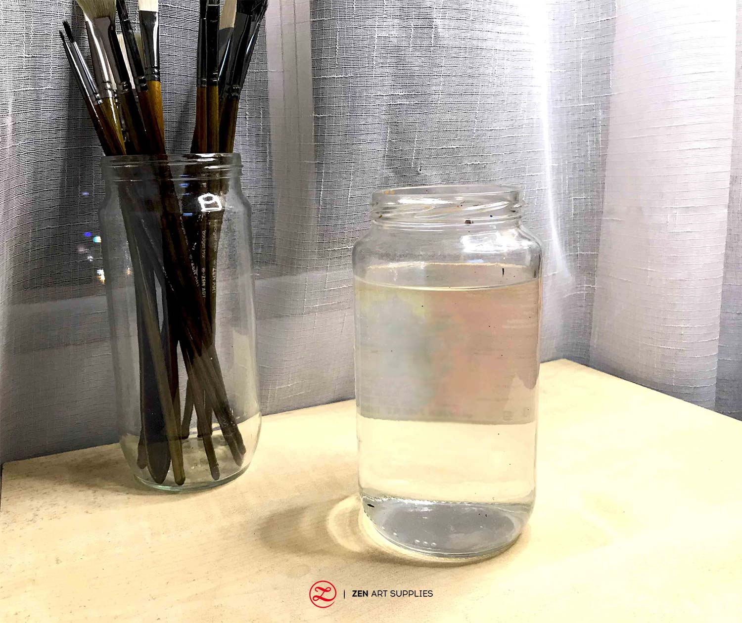 A big jar with water beside a jar holding acrylic paint brushes