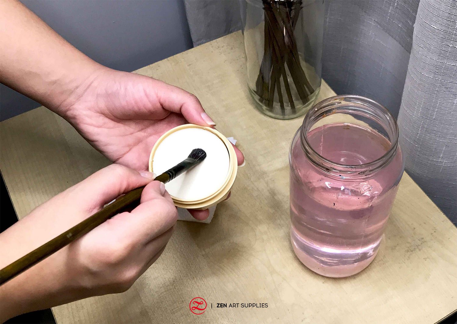 A brush being swiped on a brush cleaning soap with a jar of water beside it