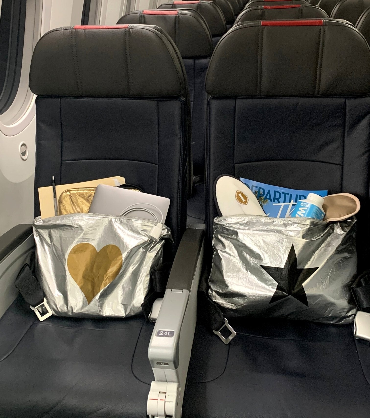 Two jumbo zipper pouches sitting on airplane seats holding laptop and departures magazine