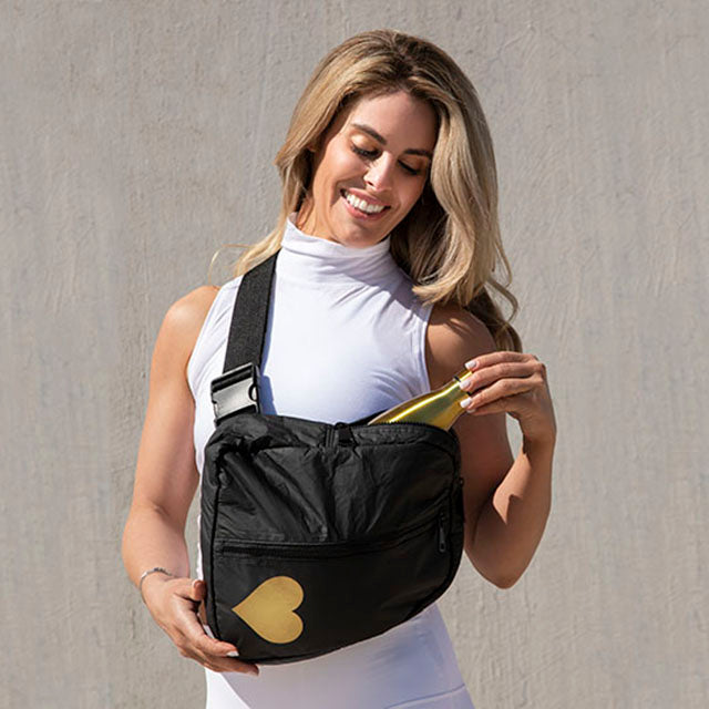 Woman in white exercise tank pulling gold water bottle out of a black crossbody backpack