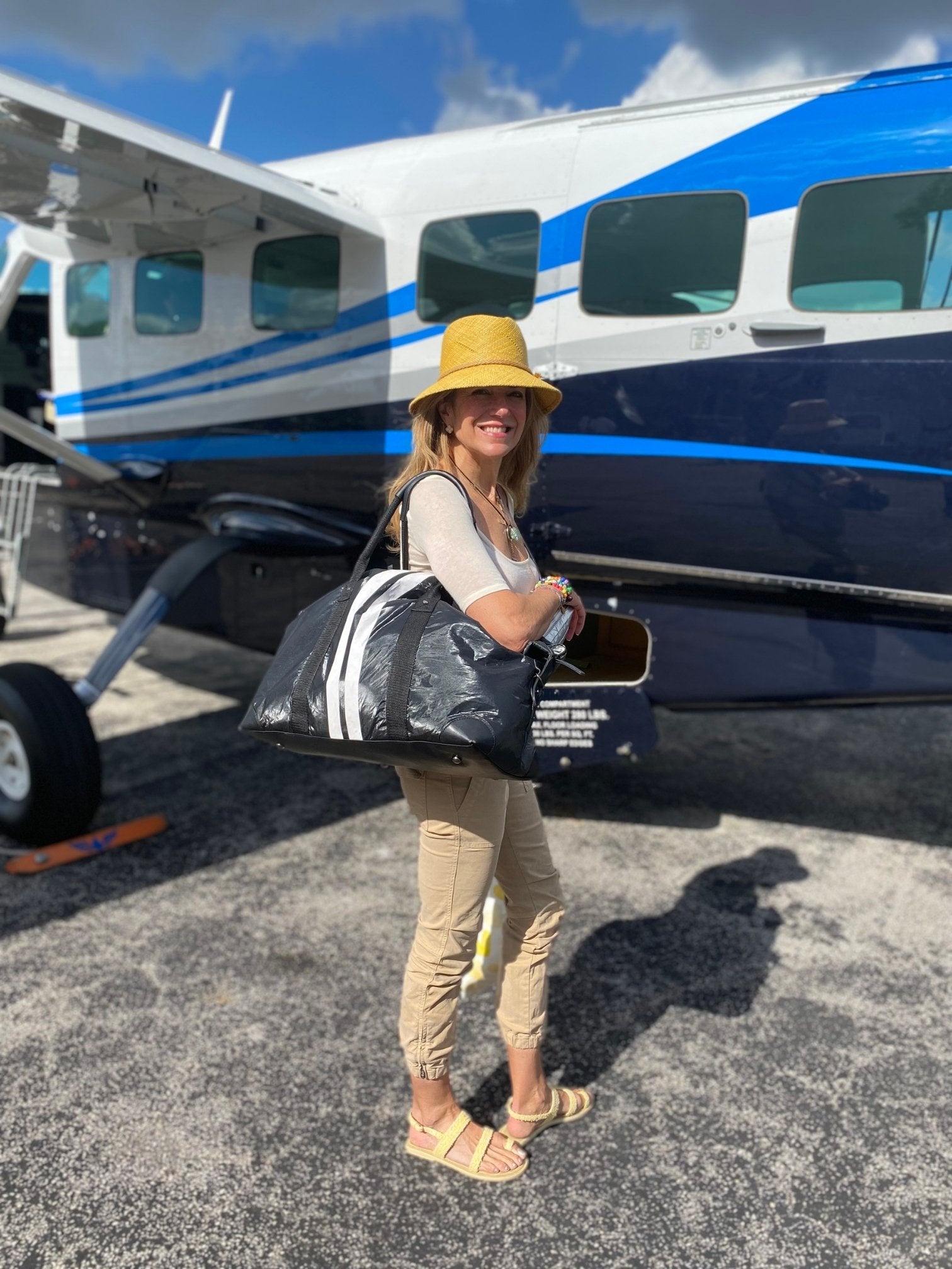 Woman standing in front of small plane with shimmer black weekender bag