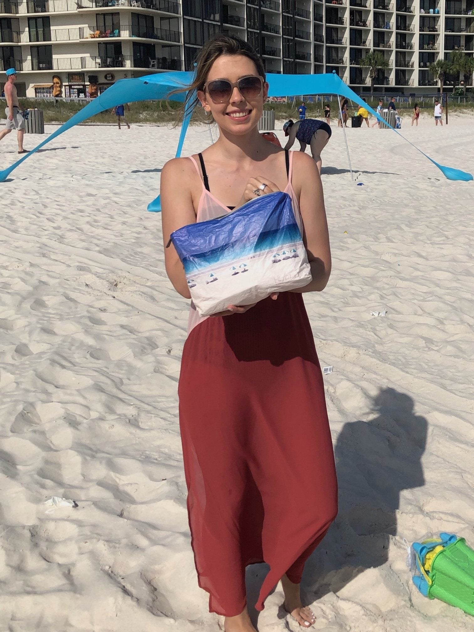 Smiling woman on a beach holding a medium size beach scene zipper pouch