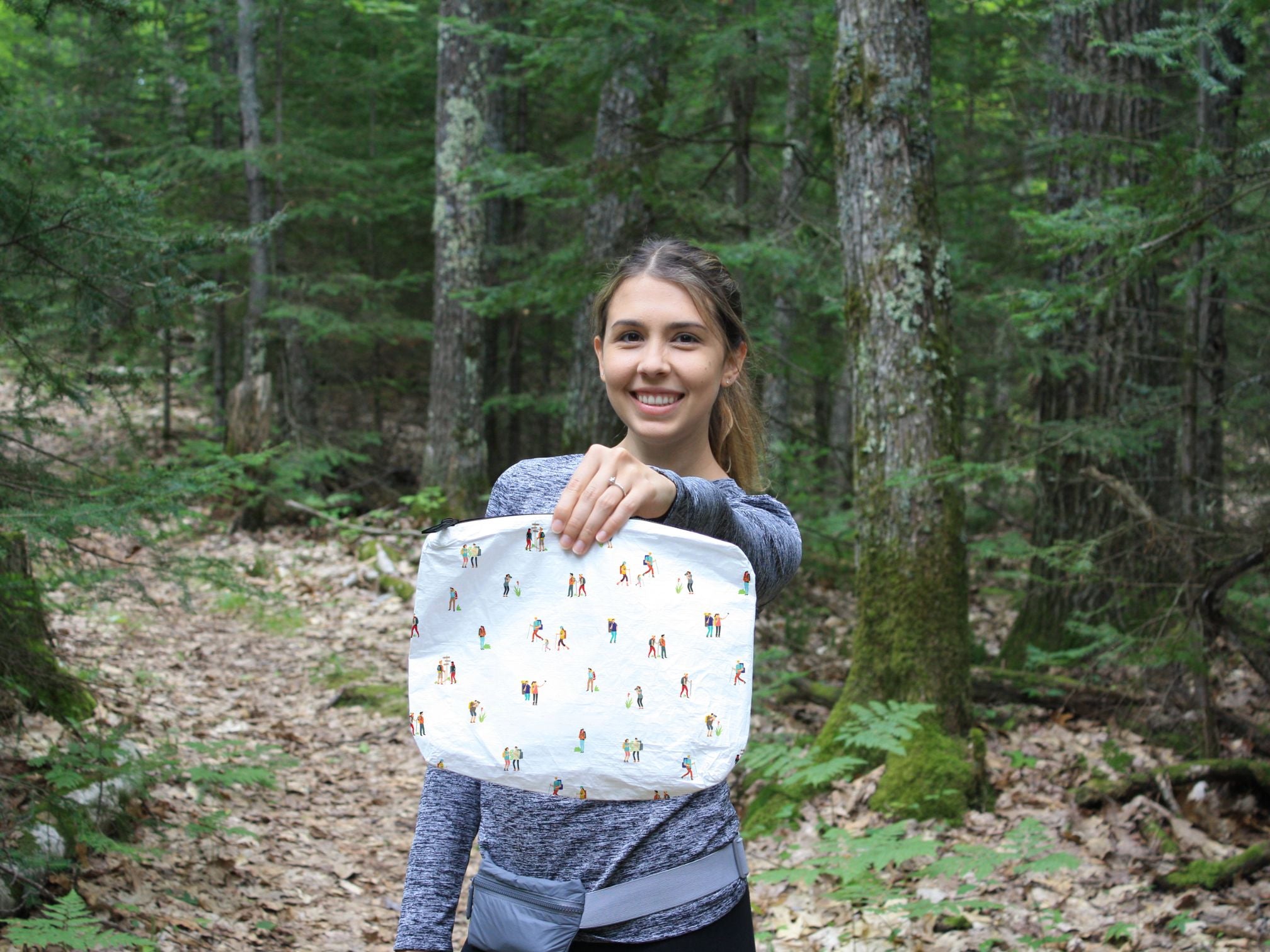 Woman standing in a forest holding a zipper pouch bag