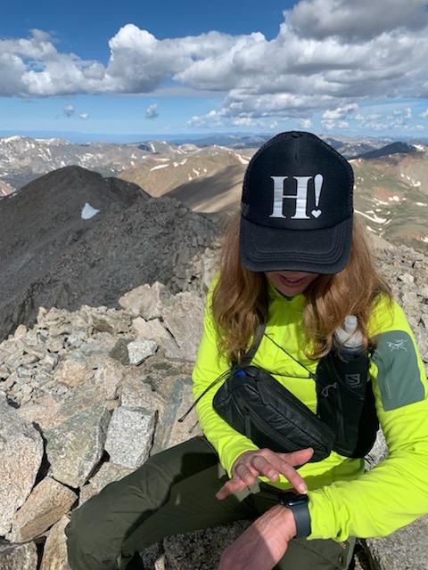 Woman sitting on top of a mountain wearing a black crossbody fanny pack