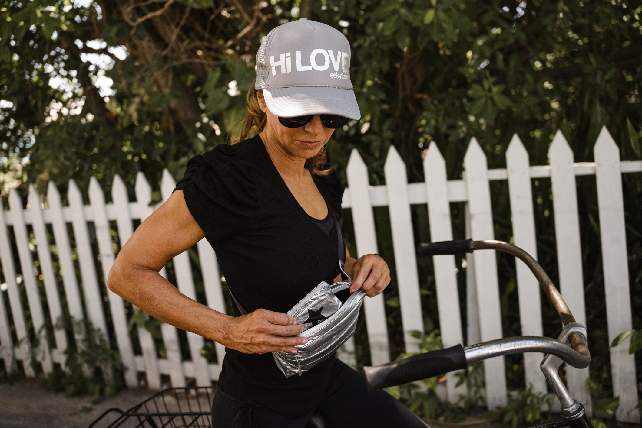 Woman wearing gray trucker hat standing on bicycle with puffer fanny pack