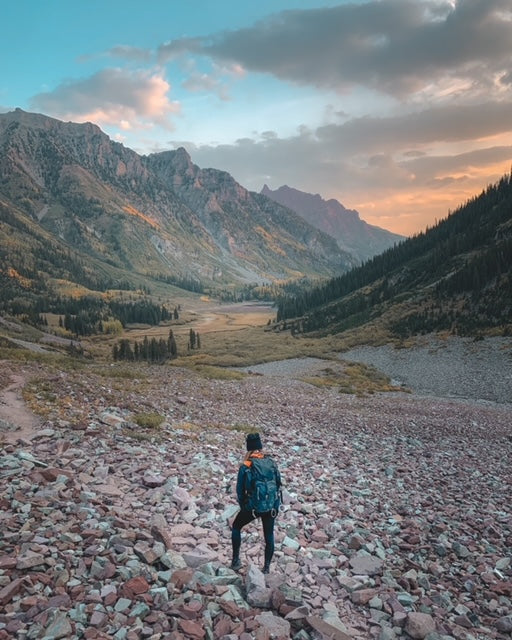 Woman standing on rocky path looking out towards Colorado mountain sunset