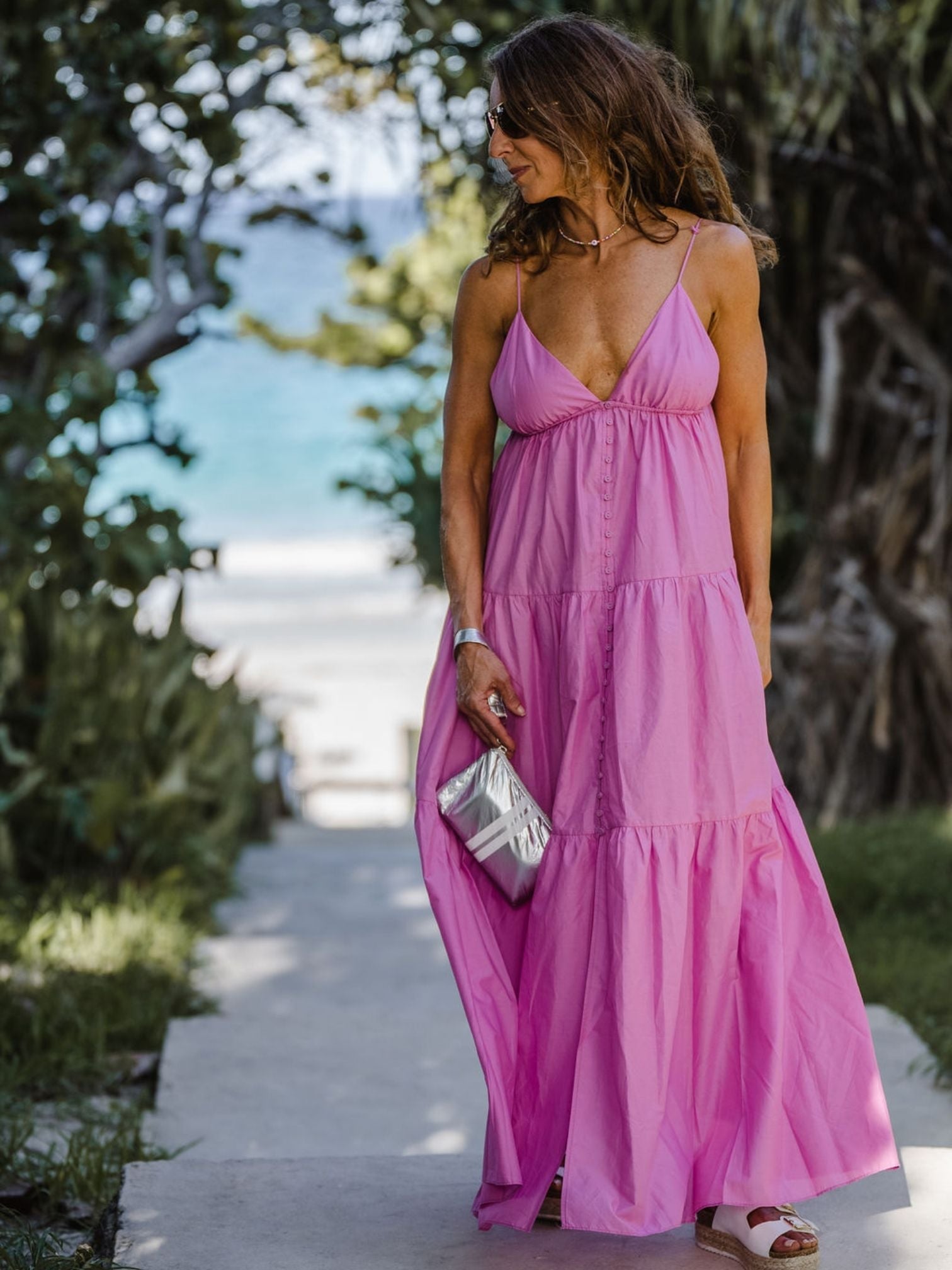 Woman standing on beach front in flowy pink dress holding silver wristlet