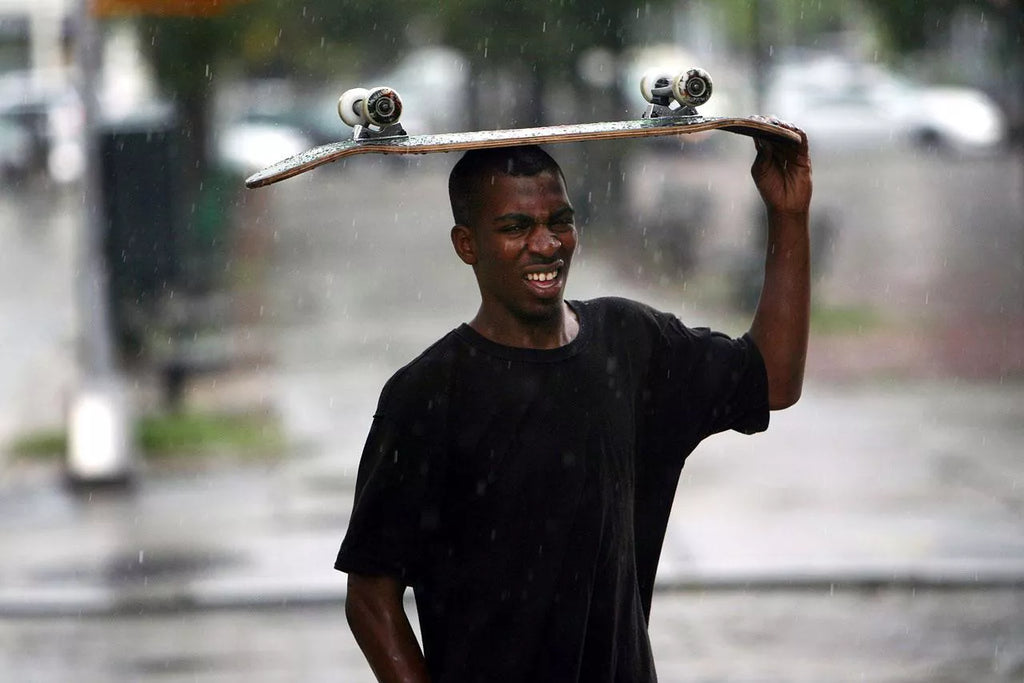 A teenager attempts to use his skateboard to keep dry during an afternoon thunderstorm