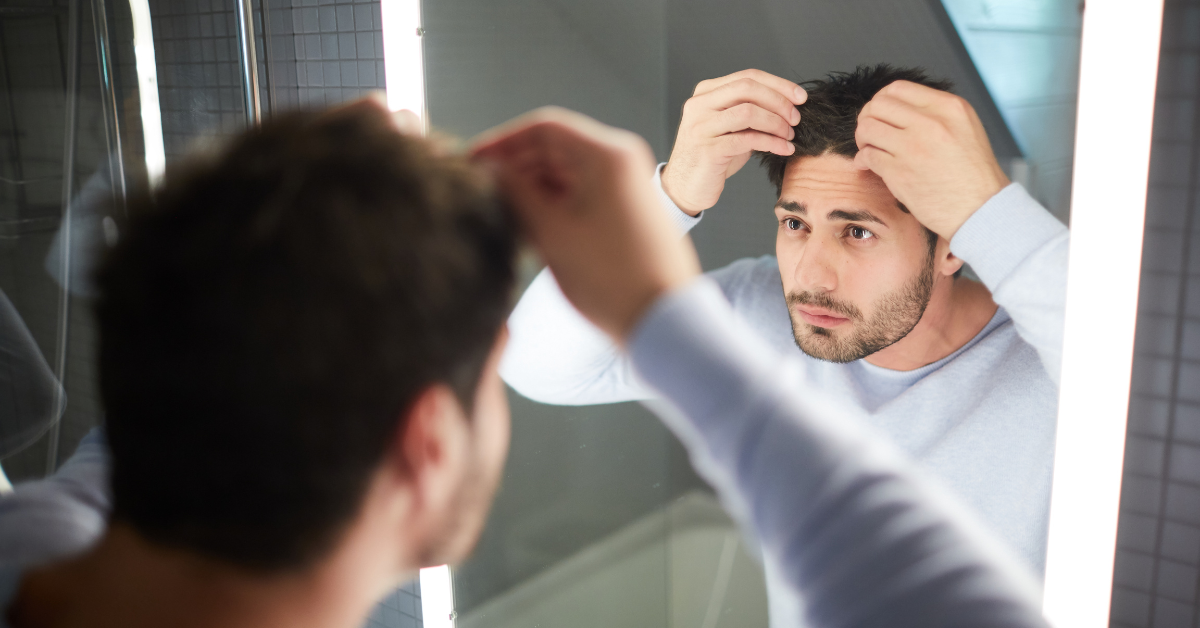 A man in the mirror checking if his hair loss is normal