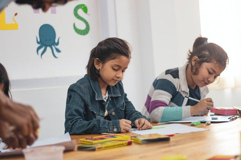 two young girls, writing in a classroom