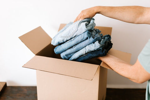 A person placing folded jeans into a cardboard box.