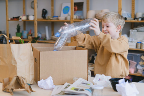 A smiling boy putting plastic bottles in a cardboard box