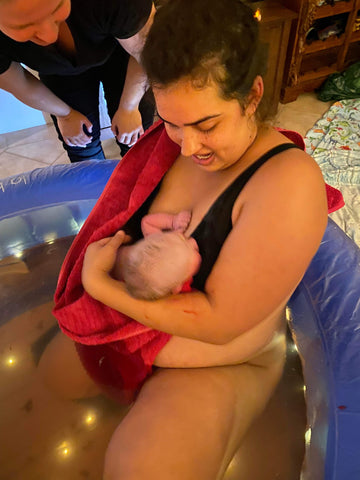 woman holds her newborn baby in the birth pool during her homebirth
