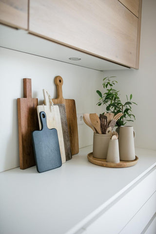 White kitchen with wooden cabinets. On the white counter top, there are wooden cutting/chopping boards and a tray with storage containers/pots/jars displaying wooden spoons and a pot plant. Interior design blog about our tips on bringing your kitchen to life without spending too much money. Written by vintage-etc in Cape Town. We make custom made & bespoke tables, benches, free-standing kitchen islands, desks, media units & wardrobes in our Cape Town & Johannesburg workshops – using Oak, Oregon, Ash, Beech, Birch Ply & Meranti. We also sell imported furniture, provide design consulting services & make soft furnishings e.g. sofas & upholstered chairs in linen, velvet & stain resistant fabric.