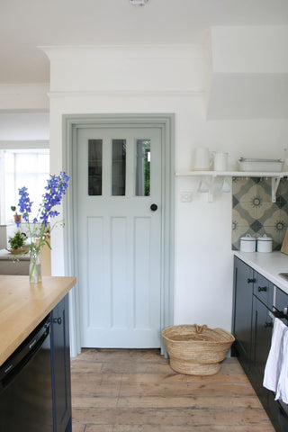 kitchen area with light blue doorway, dark blue and brown two-toned cabinets and wooden flooring.  Interior Design blog about how Europe does accent colours through two-toned cabinetry, accent ceiling and deep, dark doorways, skirting and architraves. Get the look with Vintage-etc. We make custom made & bespoke tables, benches, free-standing kitchen islands, desks, media units & wardrobes in our Cape Town & Johannesburg workshops - using Oak, Oregon, Ash, Beech, Birch Ply & Meranti. We also sell imported furniture, provide design consulting services & make soft furnishing e.g. sofas & upholstered chairs in linen, velvet & stain resistant fabric 