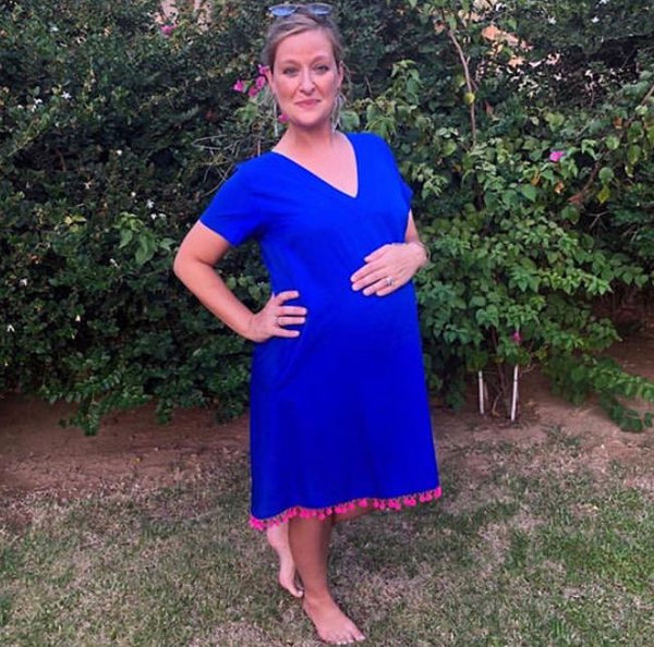 A pregnant woman wearing a blue maternity midi dress with short sleeves and a v-neckline from Neonstar standing in a home compound