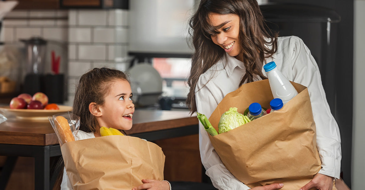 A women and child standing in a kitchen holding bags of groceries