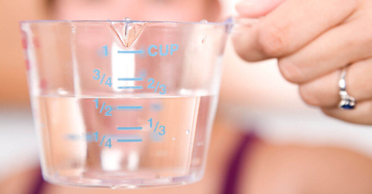 Woman's hand holding a measuring cup filled with liquid